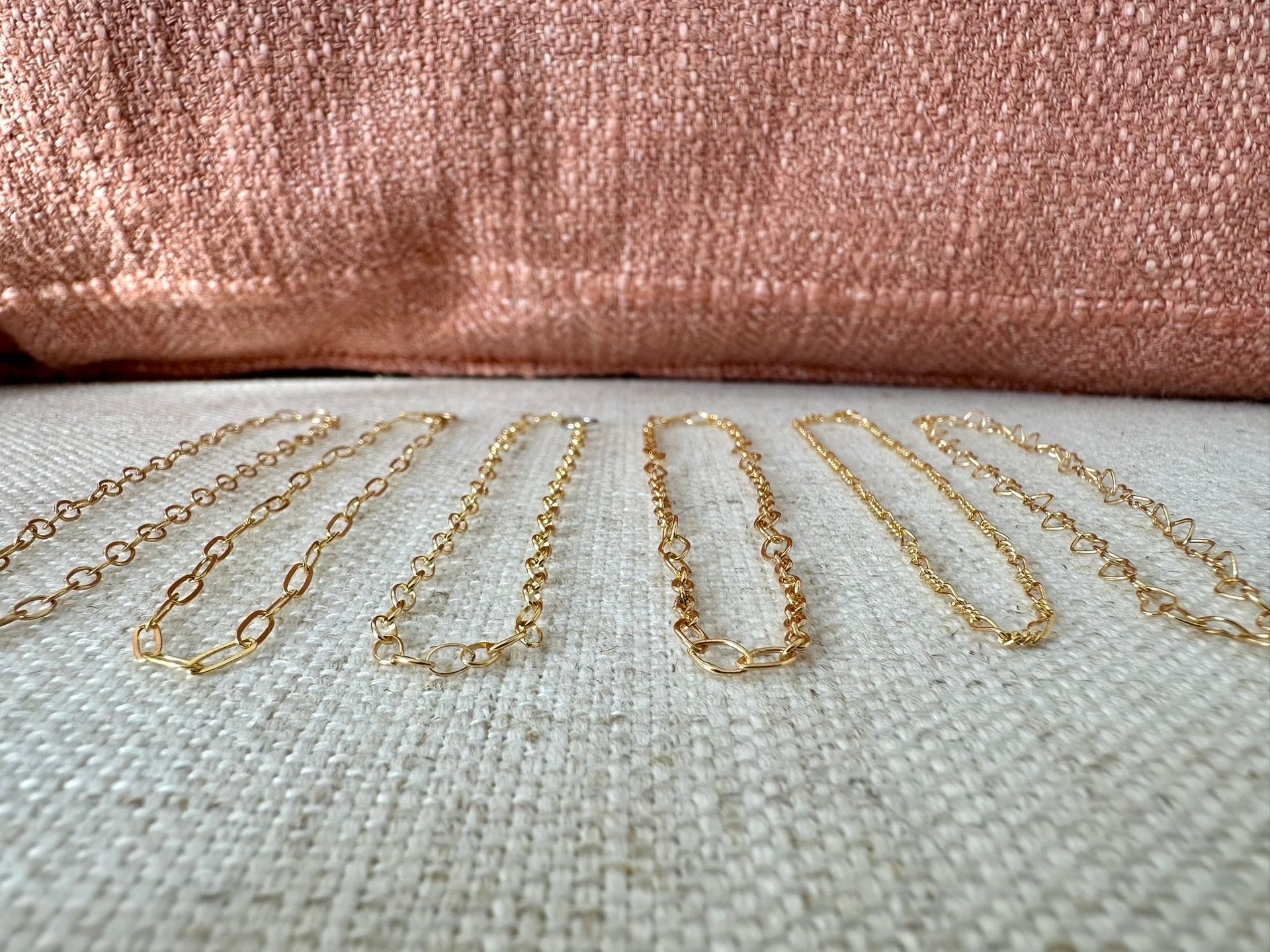 Gold chain necklaces displayed on a textured white surface, against a peach-colored backdrop.