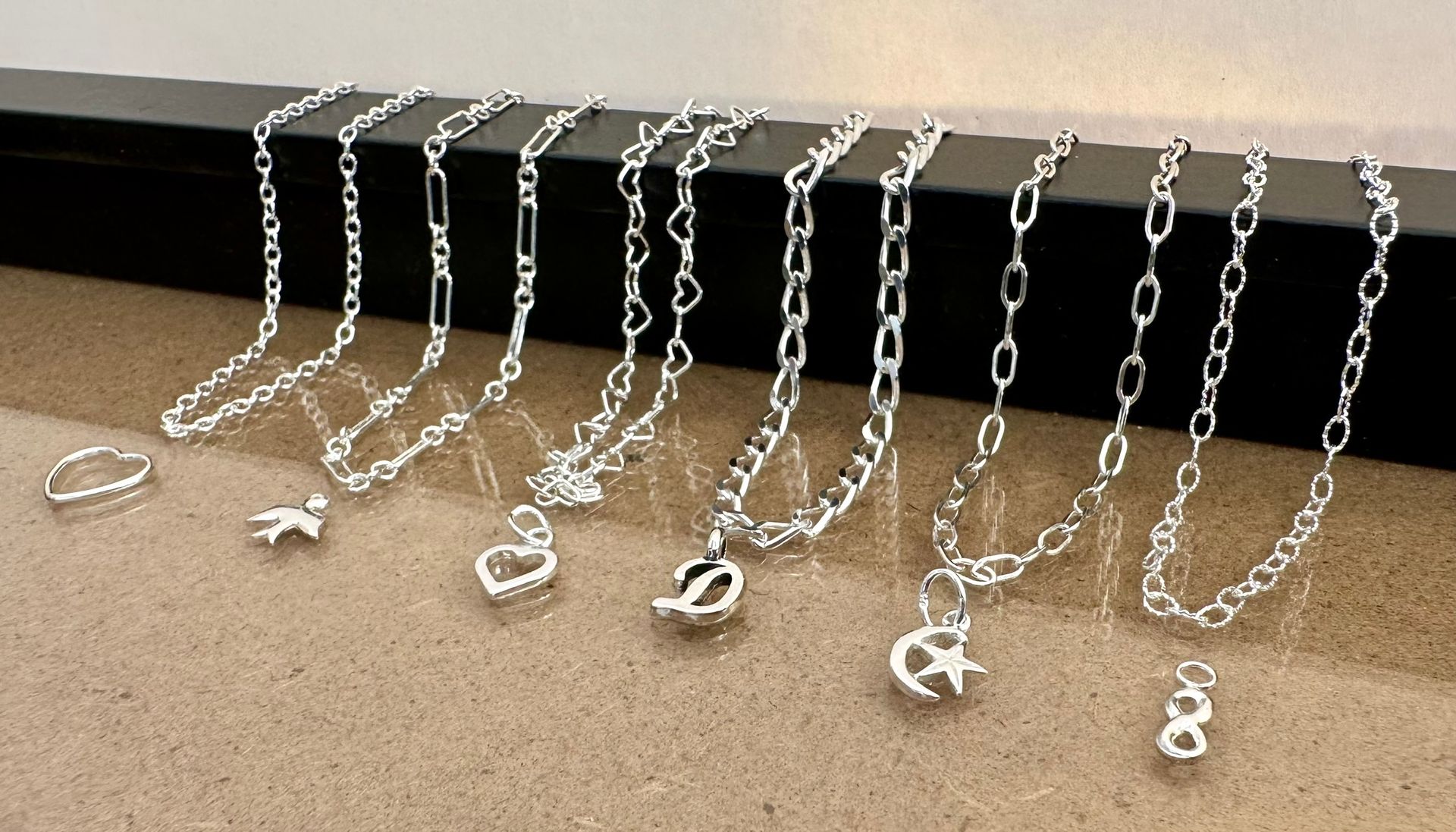 Silver necklaces and a ring on a display surface. Various chain styles with charms, including a heart, letter 