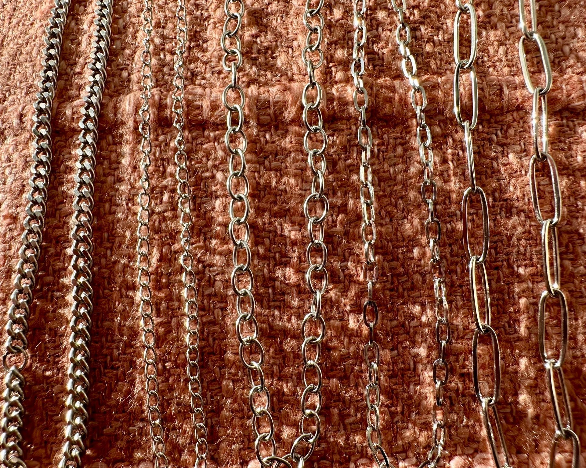 Silver necklaces of varying styles on a textured peach background.