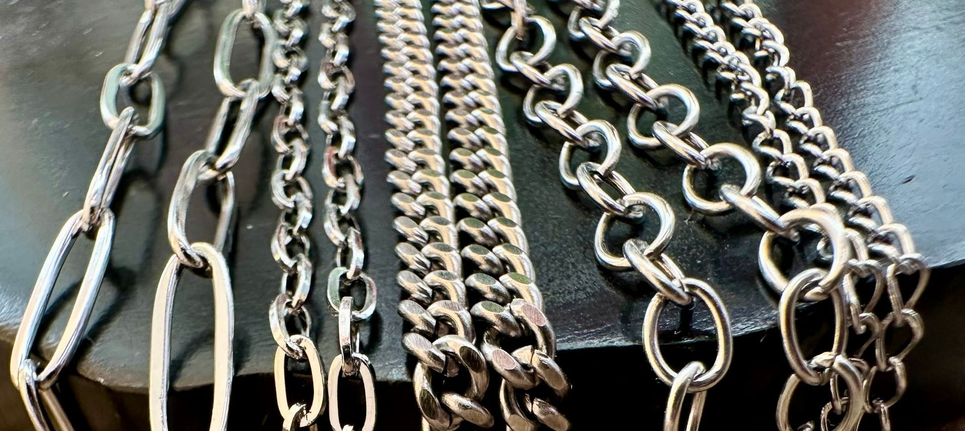 Close-up of several silver chains, different styles, on a dark surface.