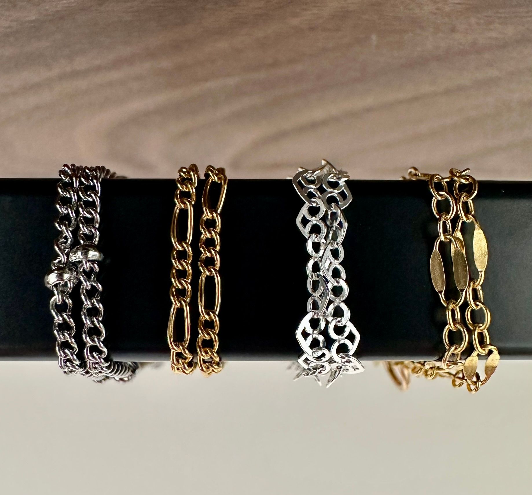 Four different chain bracelets, silver and gold, displayed on a black surface.