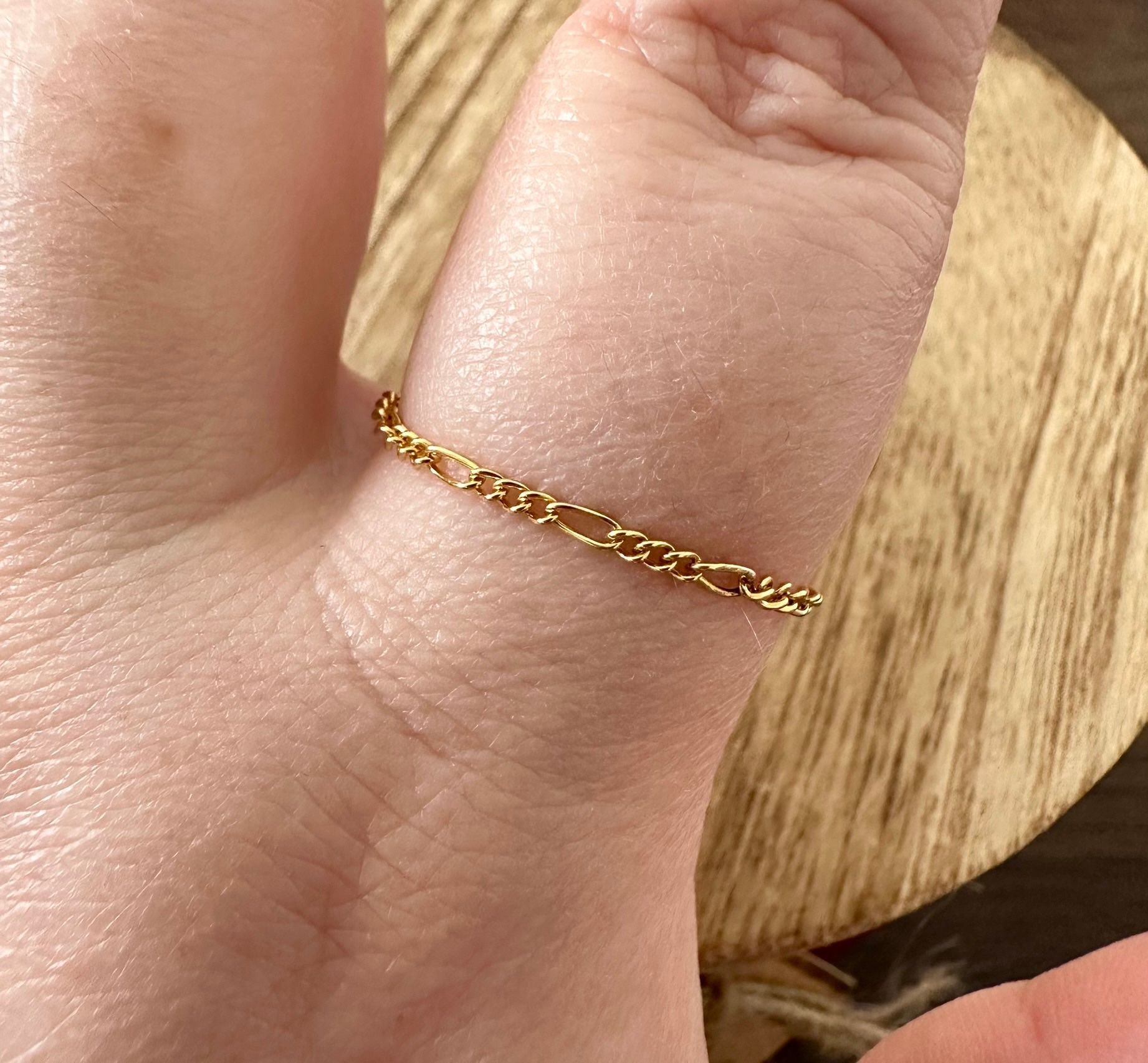 Gold chain ring on a finger, resting on a wooden surface.