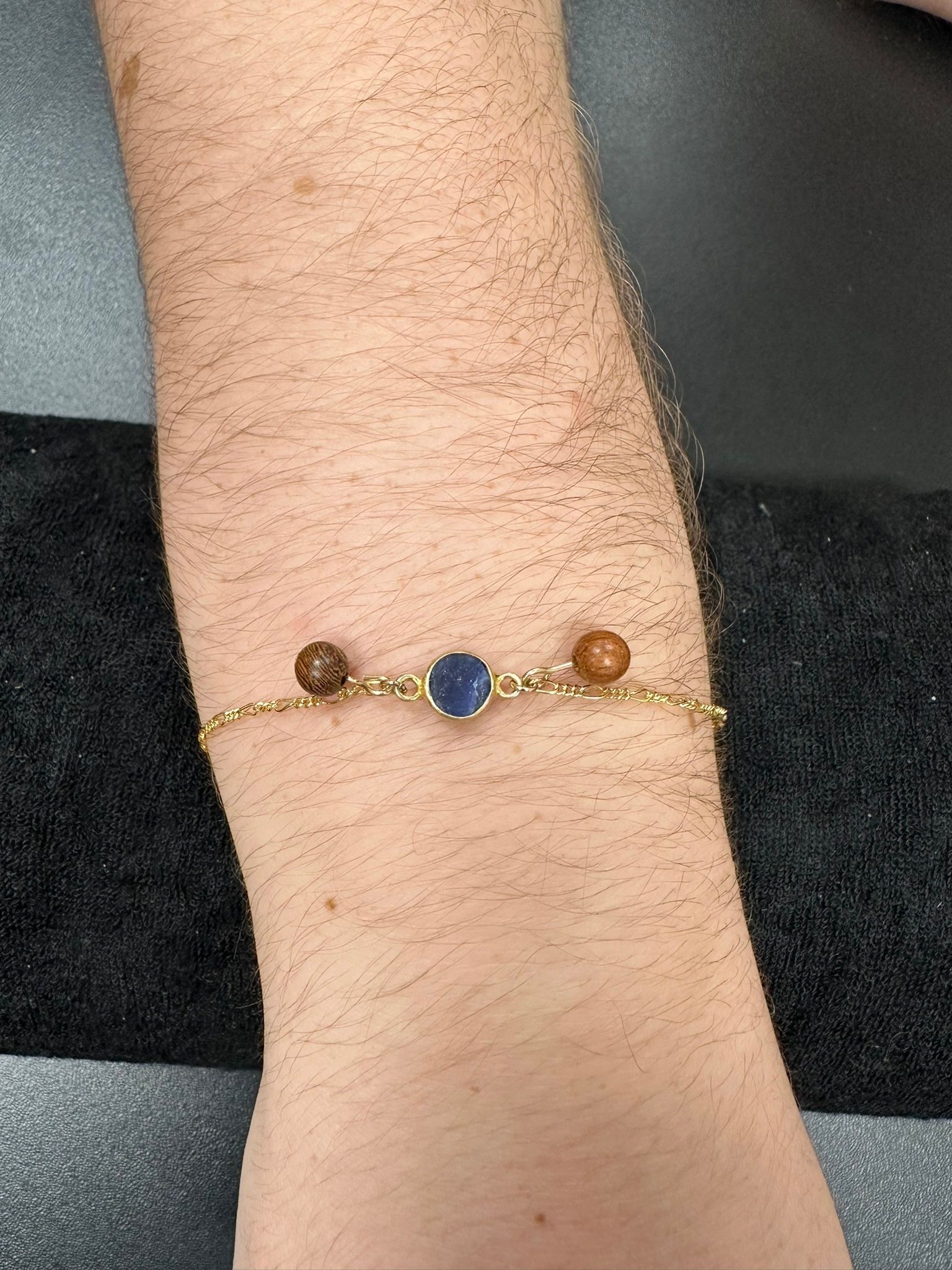 Arm with a gold bracelet featuring three beads, one blue and two brown.