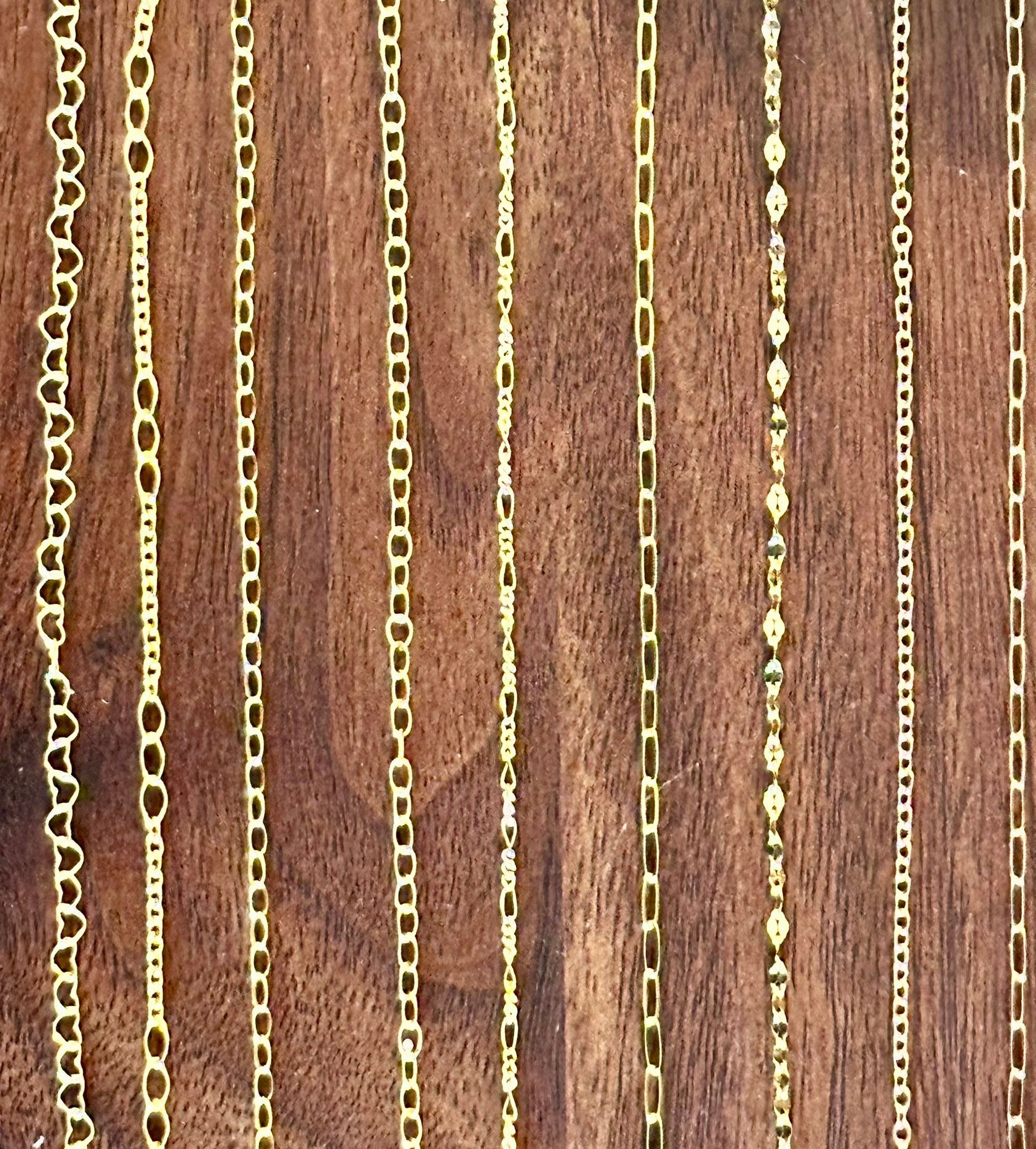 Gold chains displayed vertically against a wood background, various link styles.
