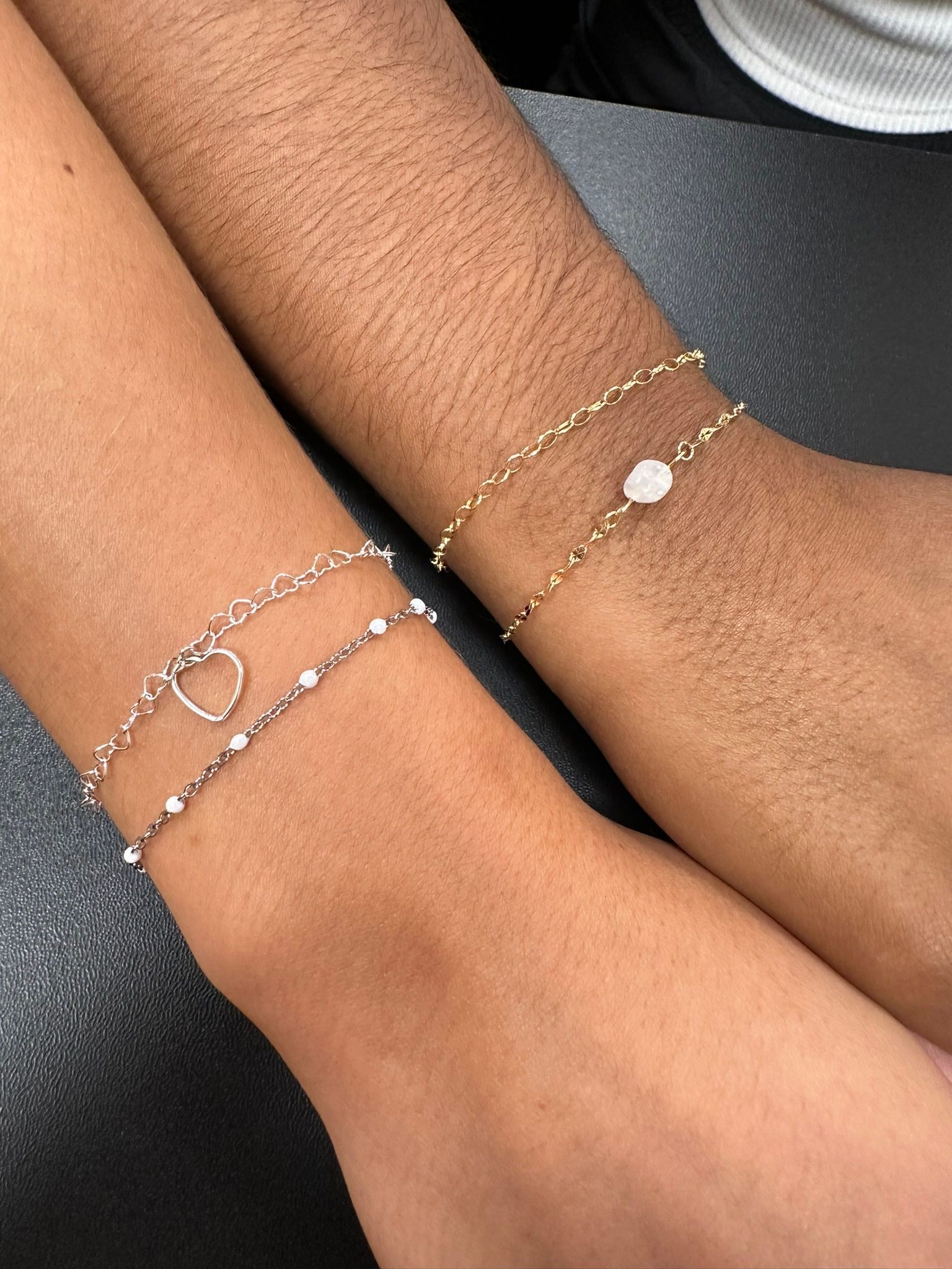 Two arms wearing delicate gold and silver bracelets.