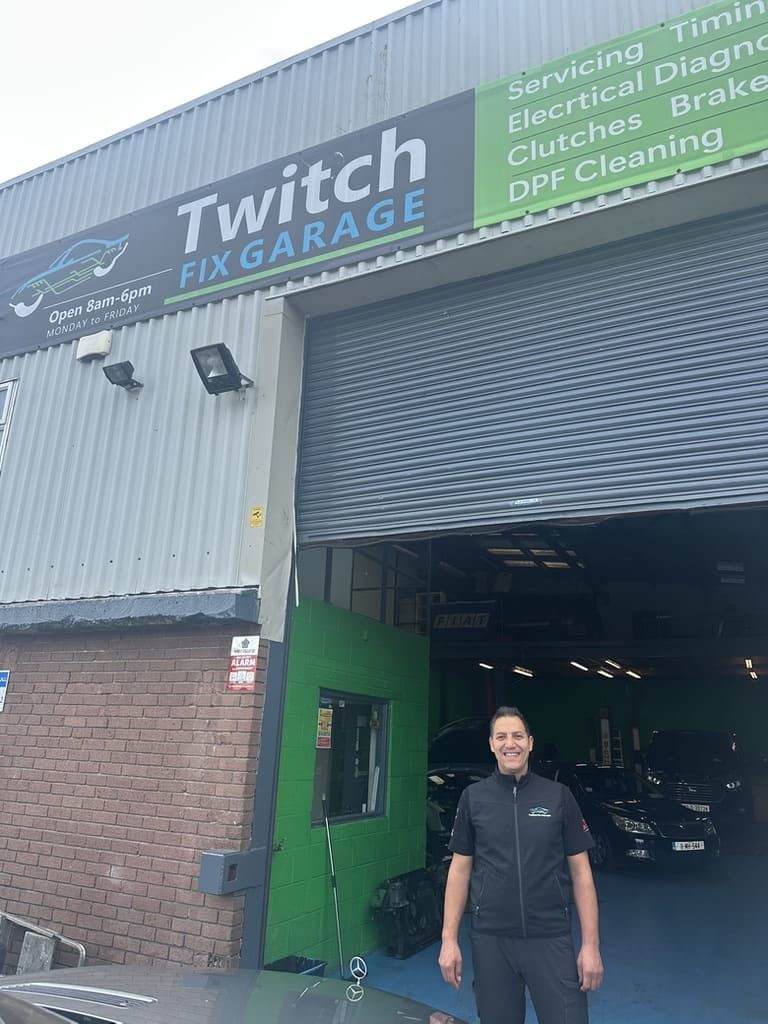 A person with arms outstretched stands in an auto repair shop with bright green walls and a blue floor.