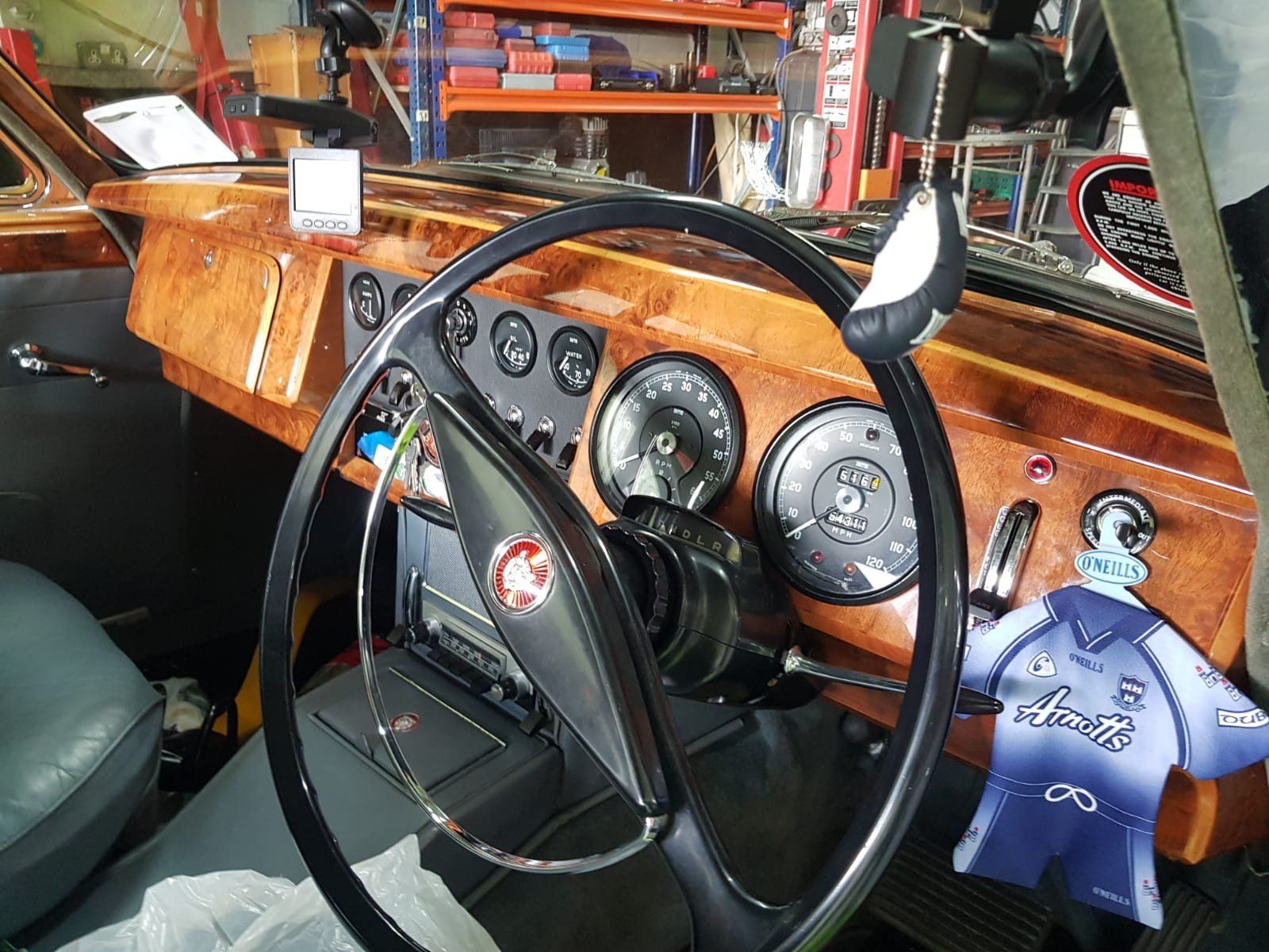 Interior of a vintage car with a wood-grain dashboard, black steering wheel, gauges, and a blue jersey air freshener.