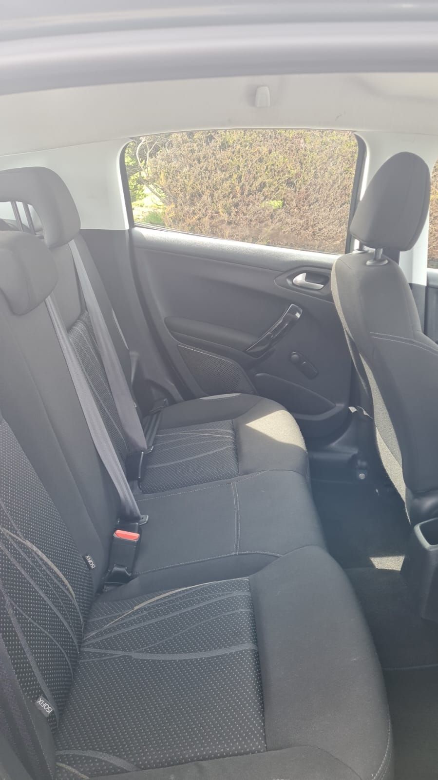 The interior back seat of a car, showing black fabric seats with a patterned design, seatbelts, and headrests.