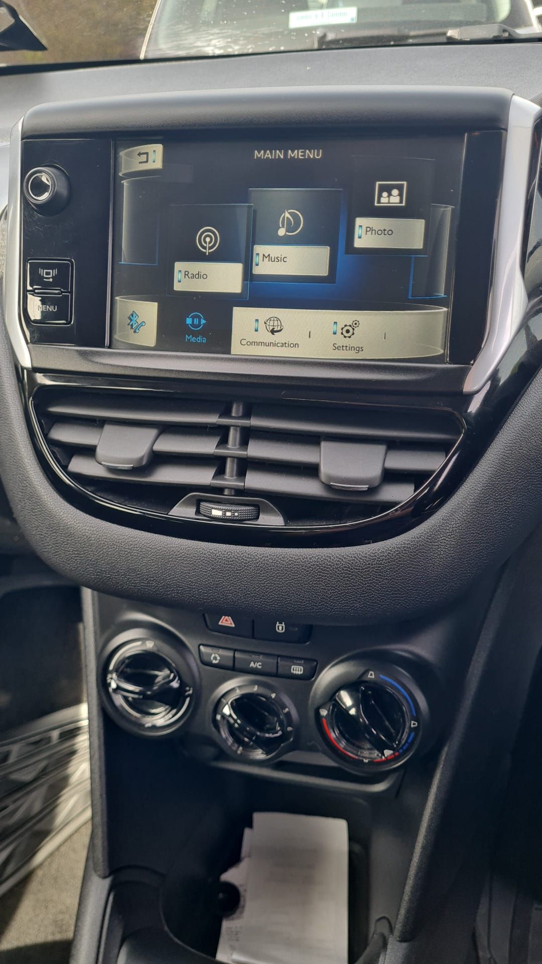Vehicle center console with an infotainment touchscreen, air vents, and manual climate control dials.