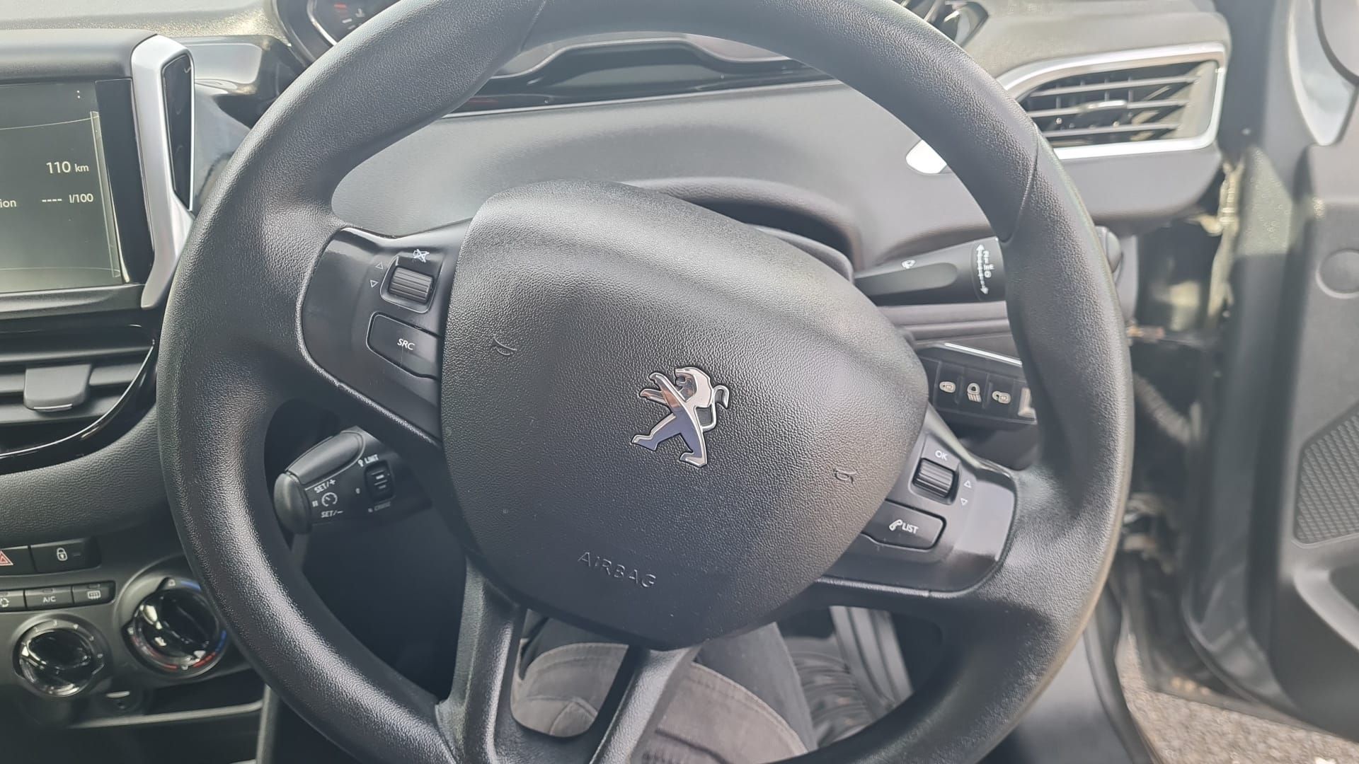 Interior of a car showing a black leather-wrapped steering wheel with a Peugeot emblem in the center.