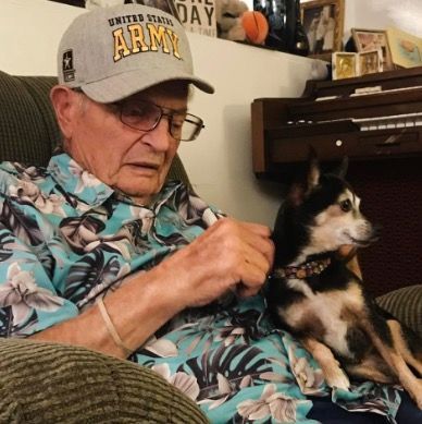 A man wearing an army hat sits in a chair with his dog