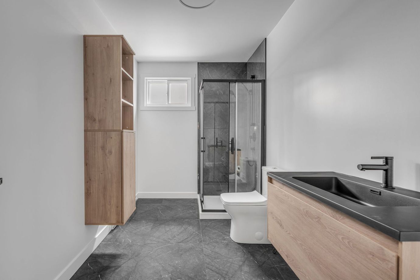 Salle de bains avec meubles en bois clair, sol gris foncé, douche et meuble-lavabo suspendu.