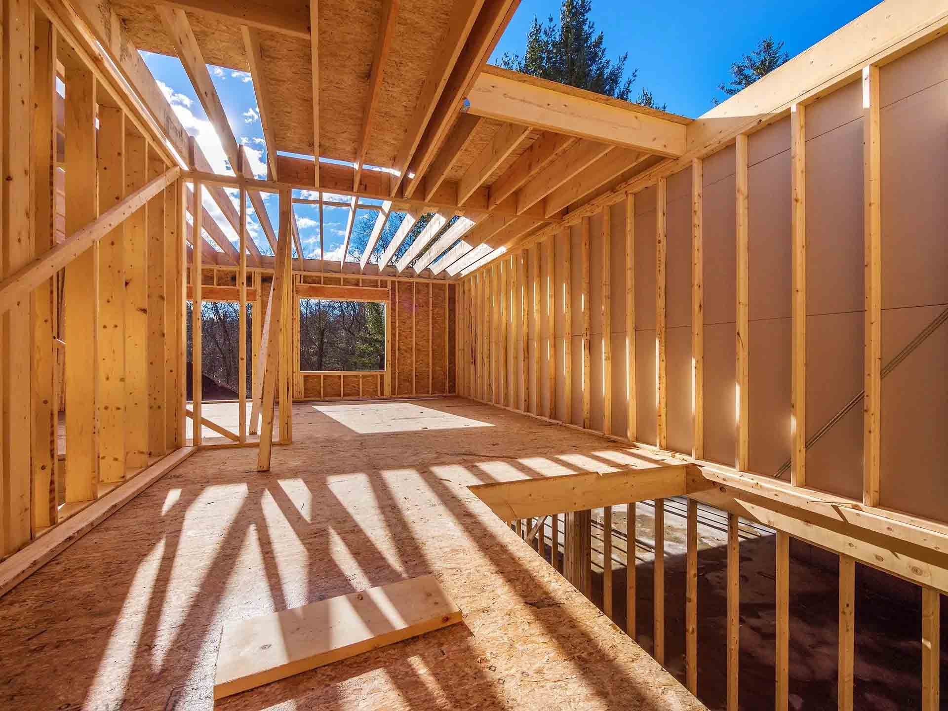 Intérieur d'une maison en construction ; charpente en bois, toit ouvert, lumière du soleil qui entre en rayon.