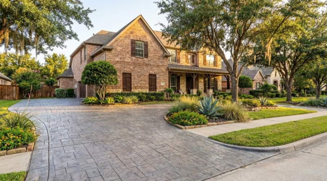 Brick suburban house with a curved driveway, landscaped front yard, and tall trees at sunset