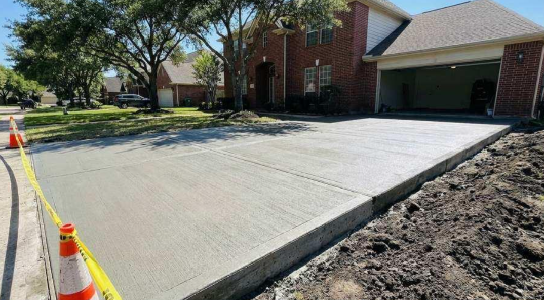 Residential driveway with fresh concrete, cones, and a brick house with garage under construction
