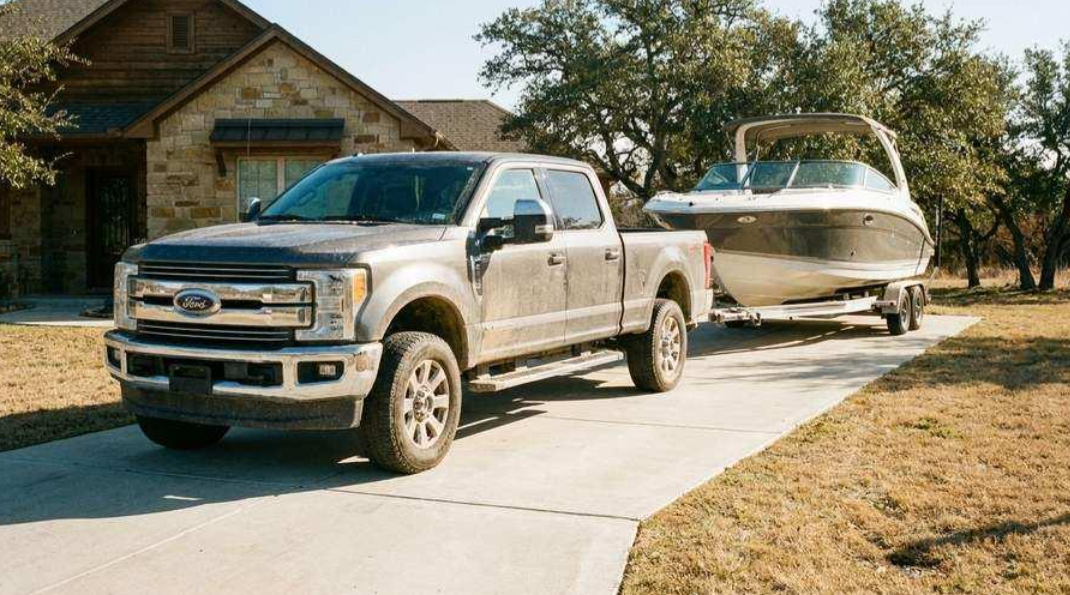 Pickup truck towing a white boat on a trailer in a suburban driveway