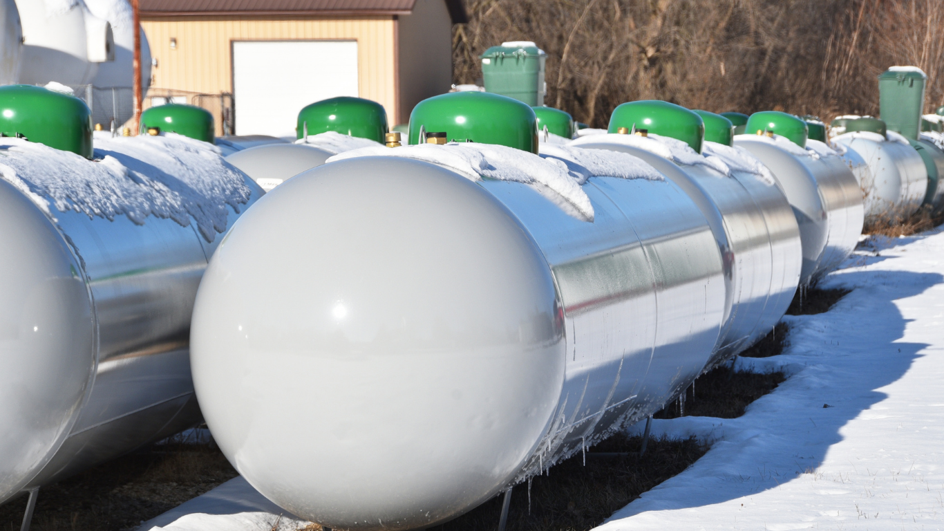 Row of silver propane tanks with green caps, covered in snow.