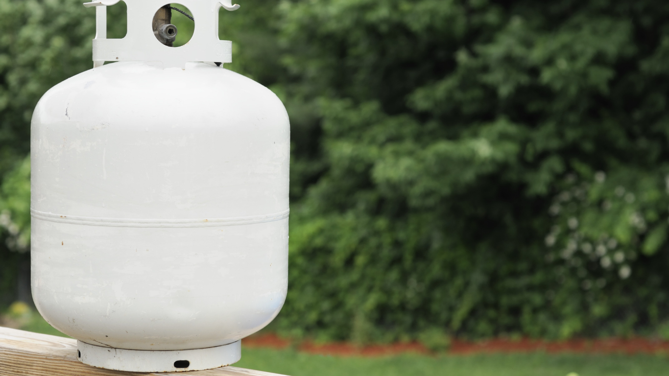 White propane tank outdoors, on a wooden surface, with a blurred green background.