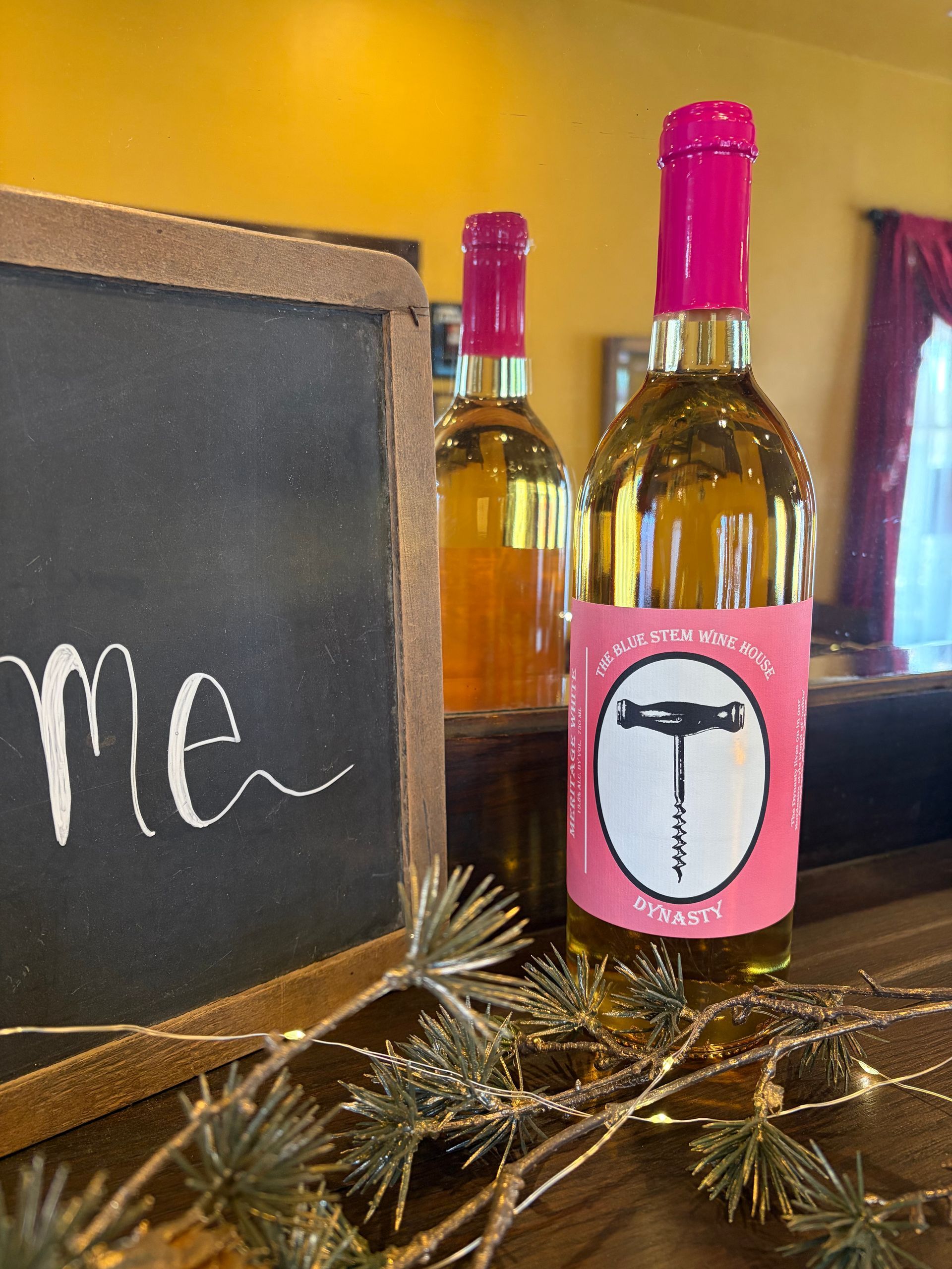 bottle with pink cap beside a chalkboard sign and dried decor on a table