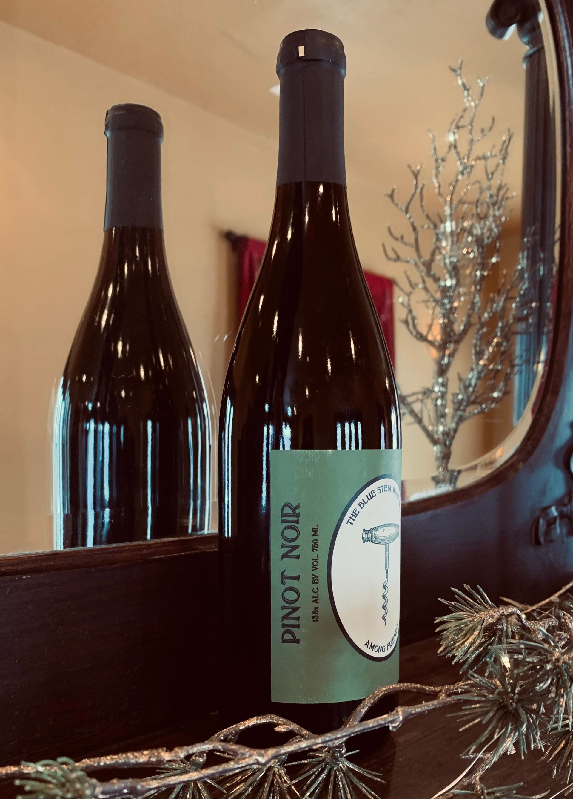 A bottle of Pinot Noir is sitting on a table in front of a mirror.