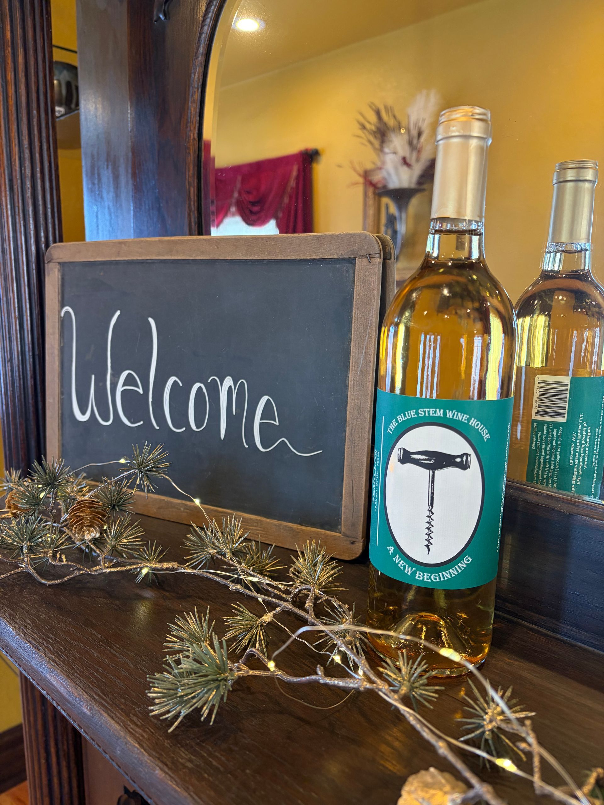Welcome chalkboard beside a bottle on a rustic table, decorated with twigs and gold accents.