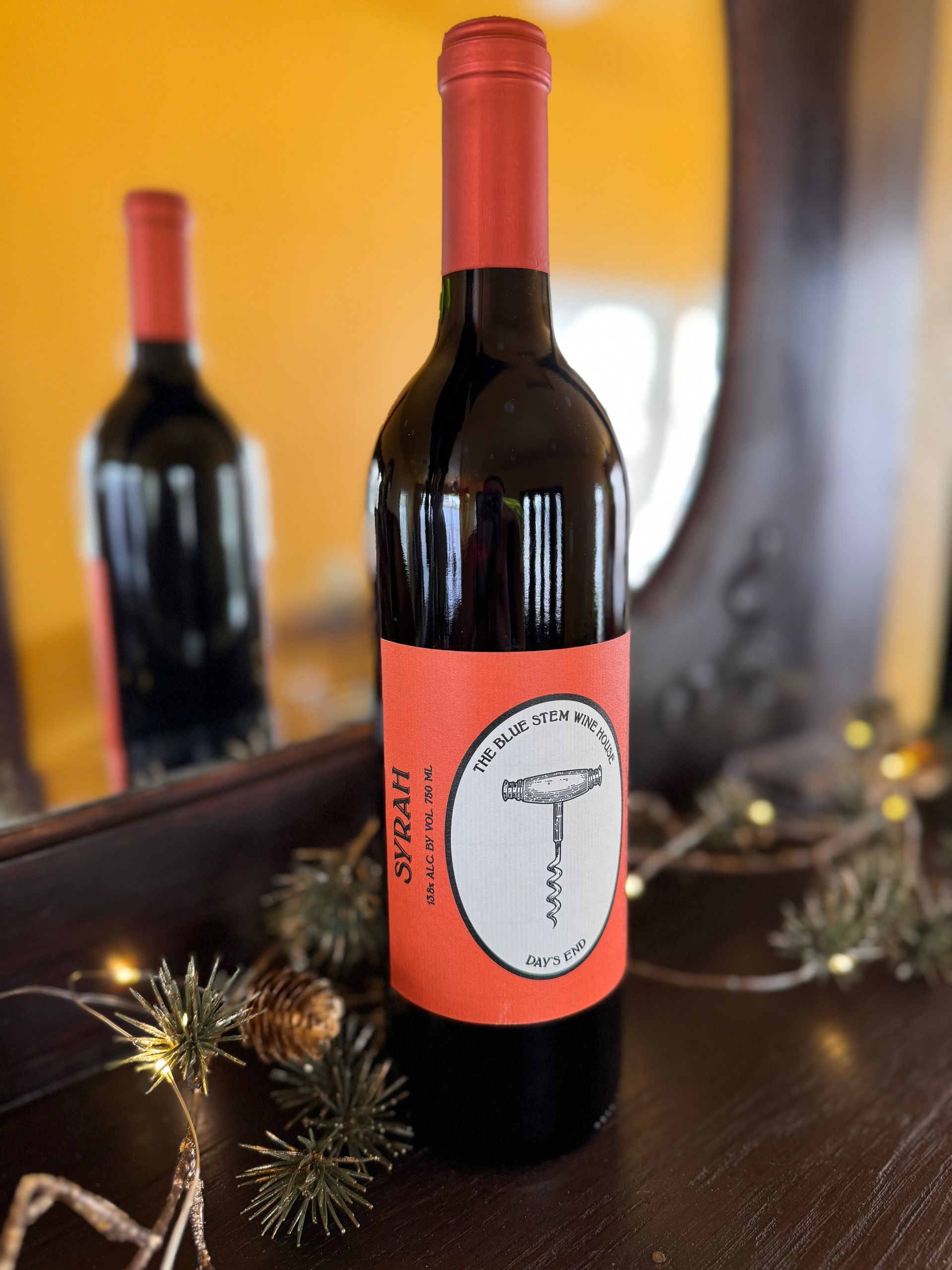 A bottle of syrah sits on a table in front of a mirror