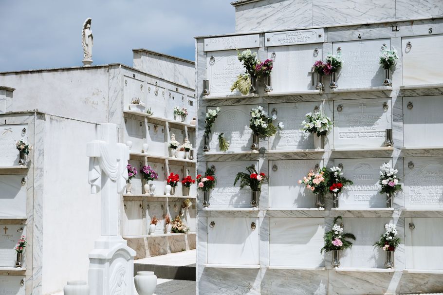 Esterno di cimitero italiano ben curato, cielo azzurro, fiori bianchi freschi