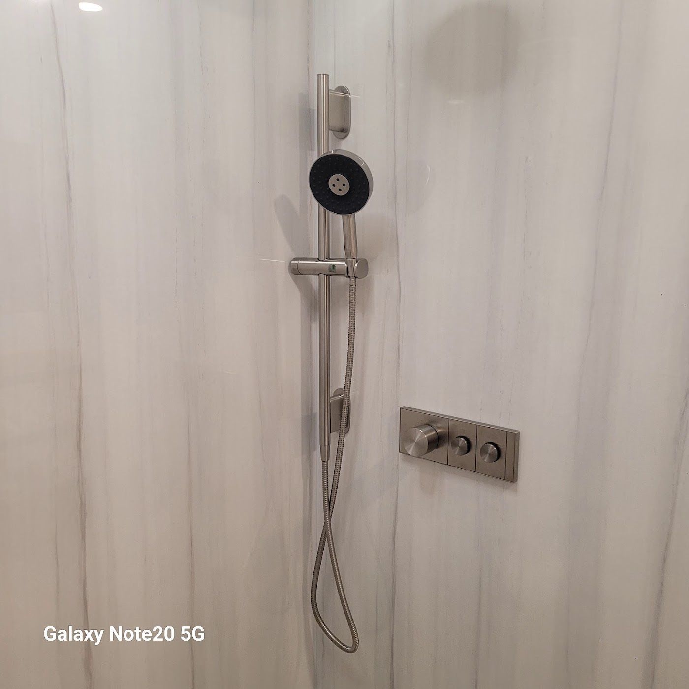 Shower with handheld showerhead and control panel on a marble-patterned wall.