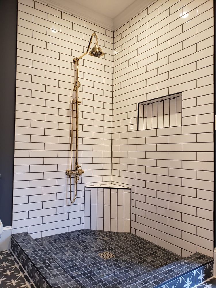 Shower with white subway tile walls, dark floor, and brass fixtures.