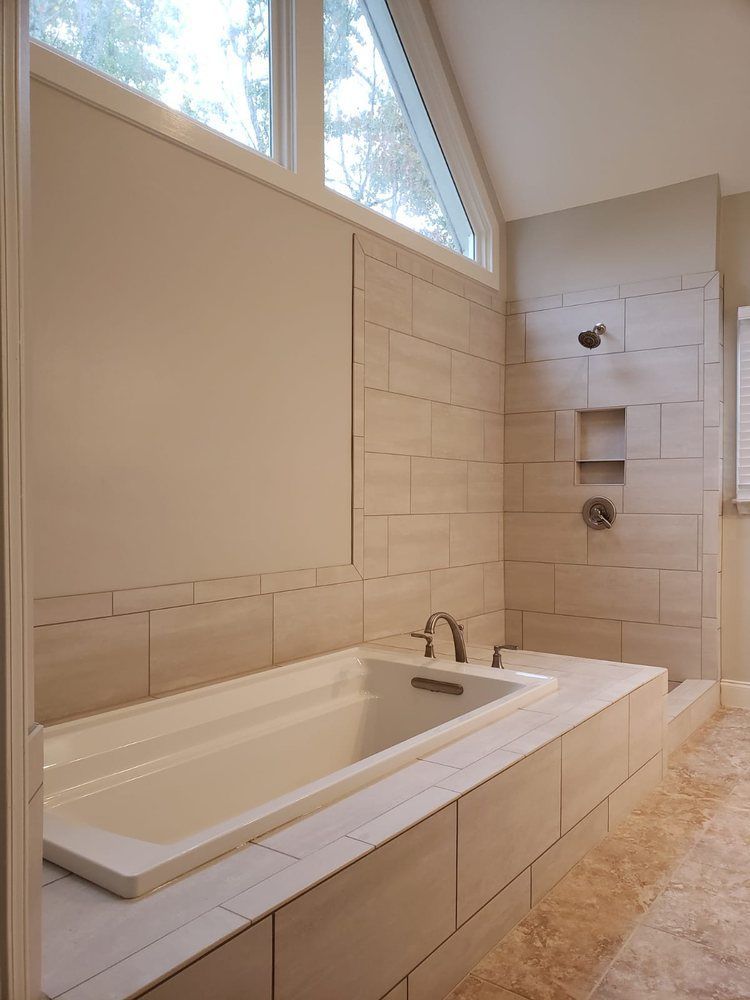 Modern bathroom with a bathtub and walk-in shower. Beige tile, white tub, and window.