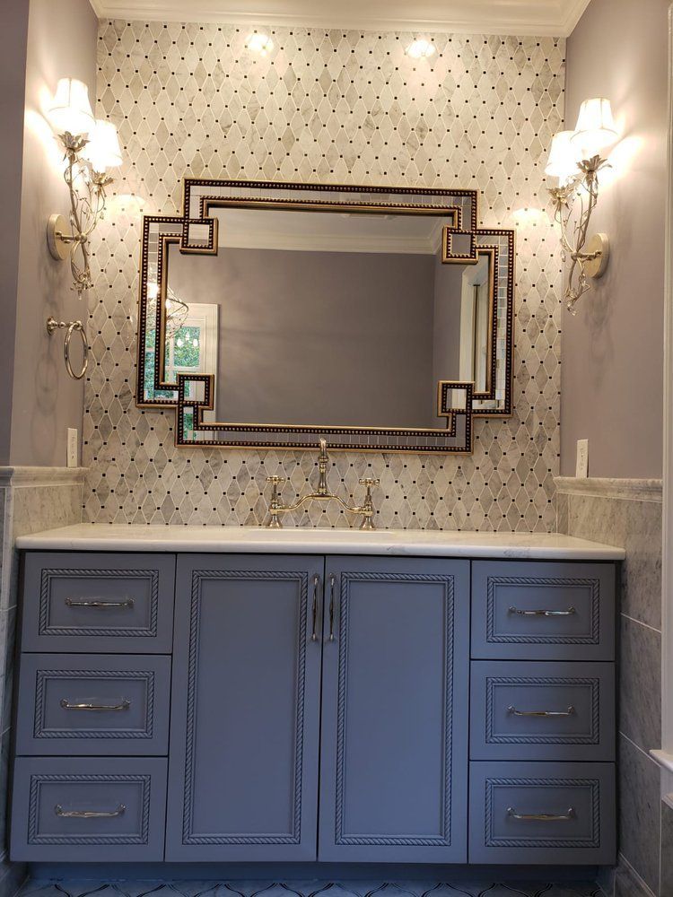 Gray bathroom vanity with mirror, sconces, and patterned wallpaper.