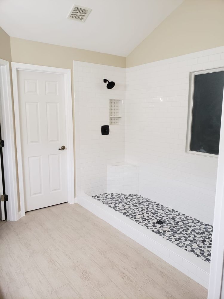 Bathroom with white walls, black shower fixtures, pebble floor, and white door.