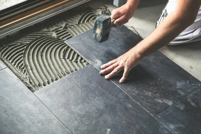 Person installing dark tile flooring, using a mallet to secure a tile.