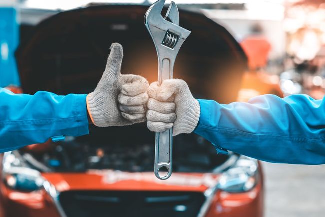 Two gloved hands holding a wrench in front of an open car hood
