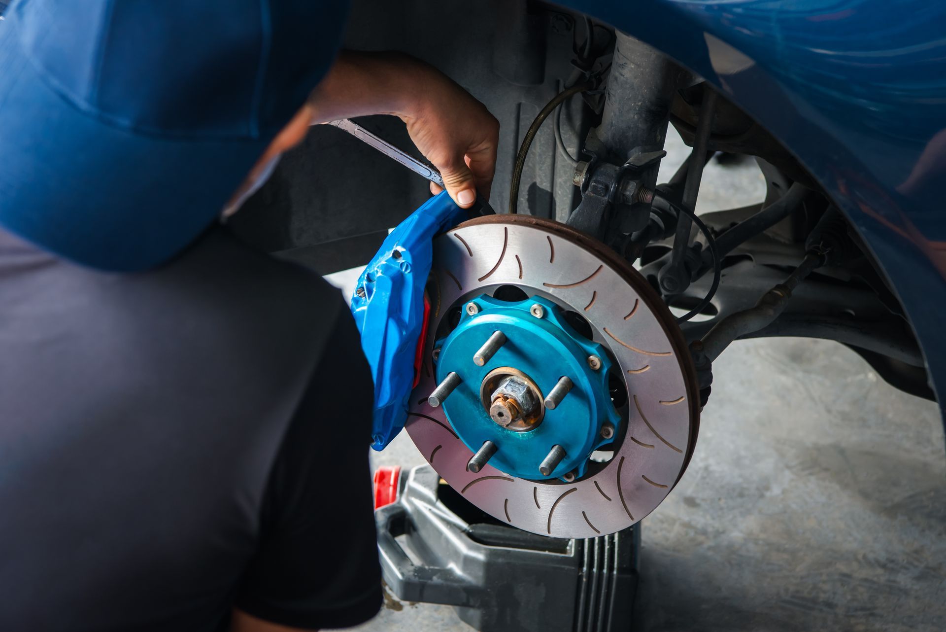 Mechanic working on a car’s blue brake rotor and wheel assembly in a garage