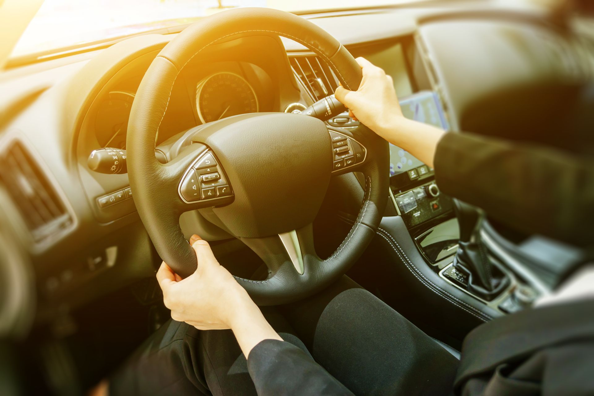 Hands on a steering wheel inside a car, driving in bright sunlight