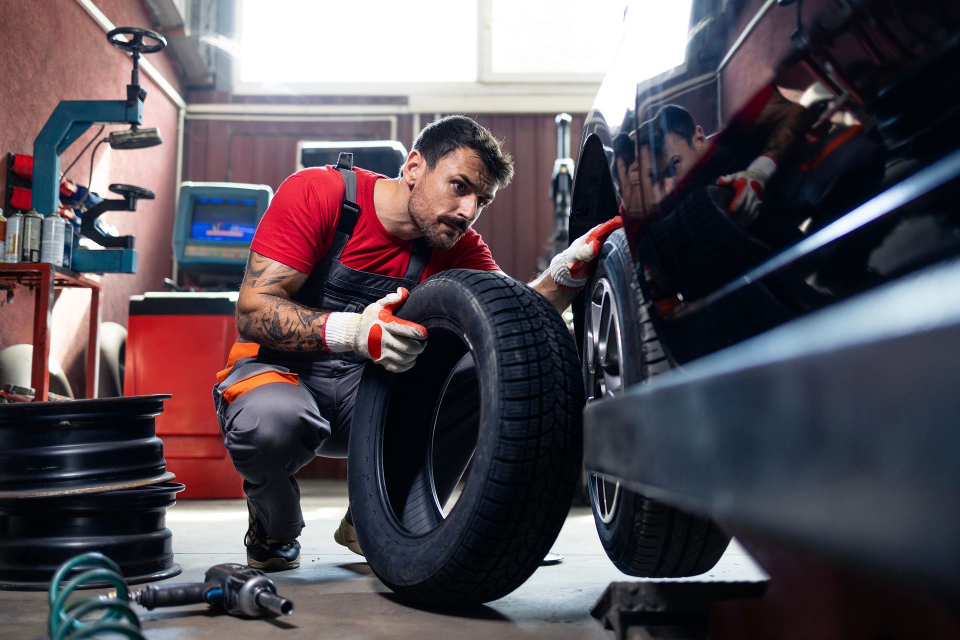 Mechanic in red shirt installing a tire on a car in a garage