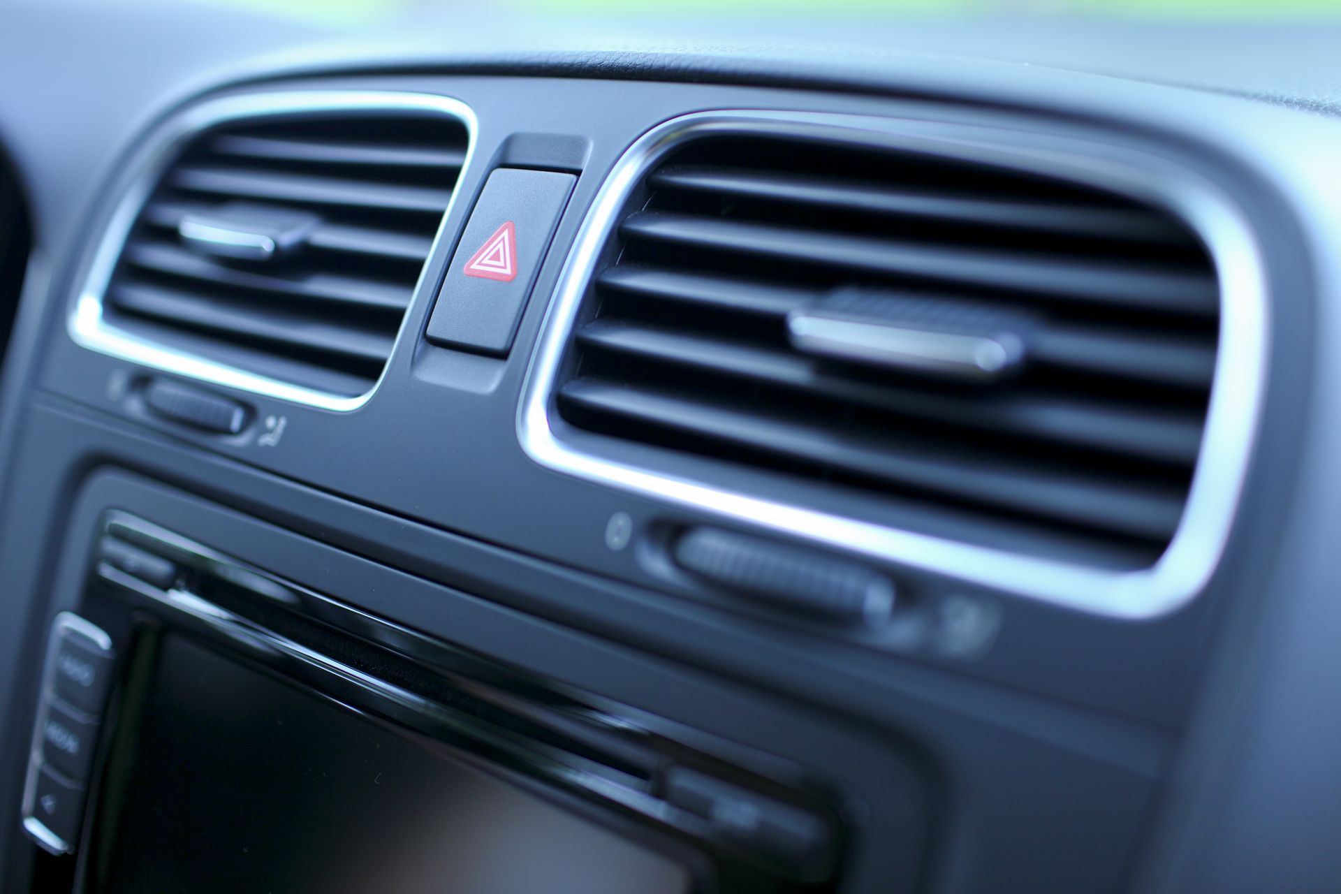 Car dashboard center vents with a red hazard light button and infotainment screen below
