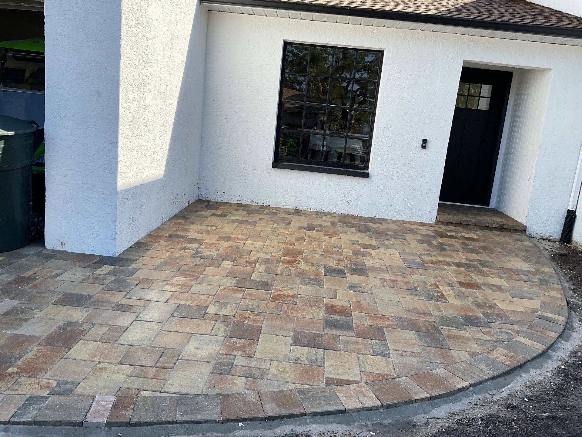 Curved brick-paver patio beside a white house with a window and dark front door