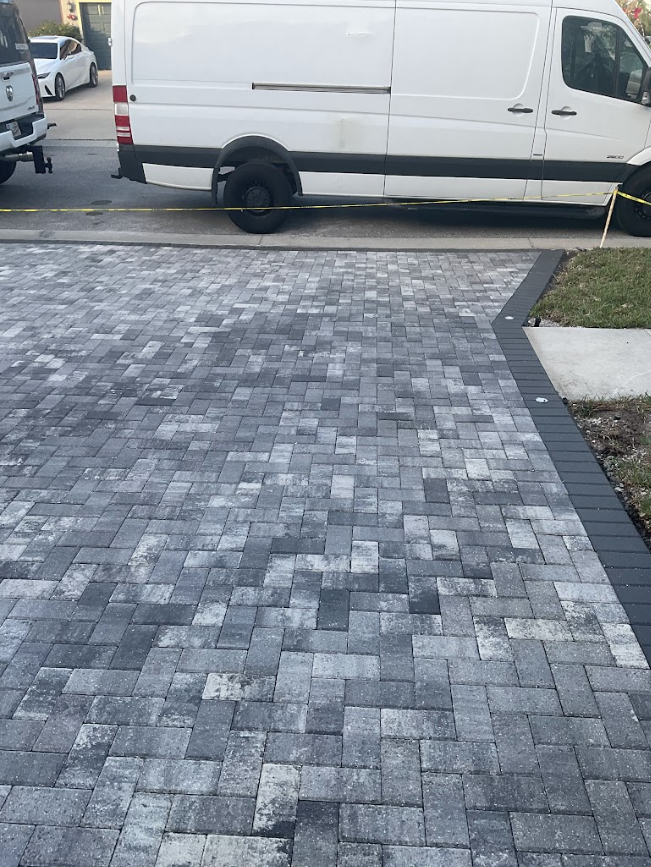 Gray paver driveway in front of a white van parked along the street