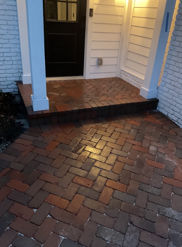 Brick walkway and small front porch with black door and white siding at dusk