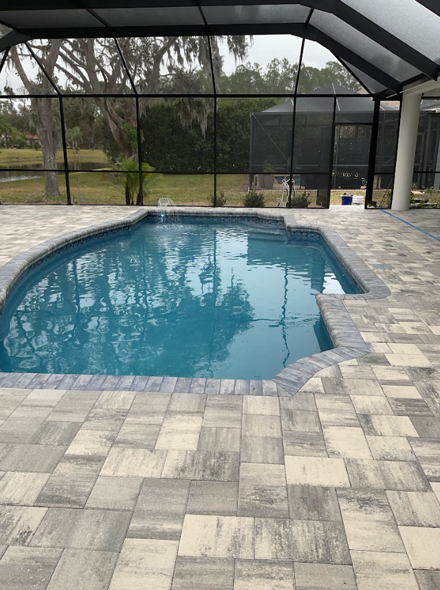 Screened-in backyard pool with blue water and gray paver patio