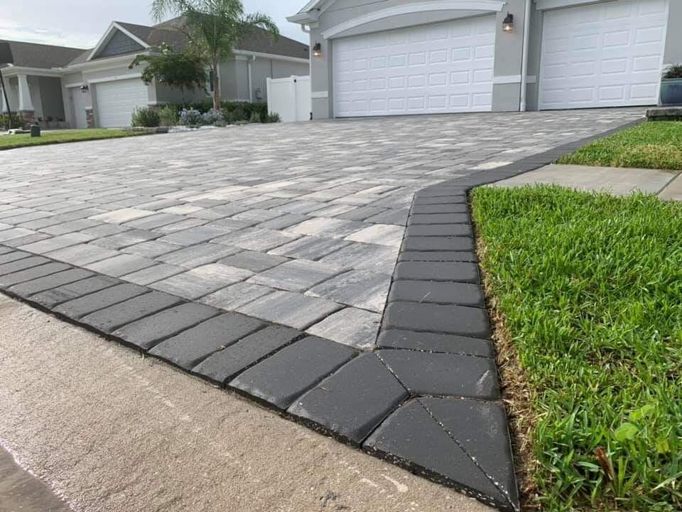 Paver driveway beside a green lawn and suburban garage doors.