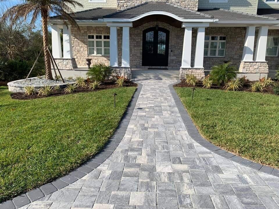 Stone walkway leads to a home’s front entrance with green lawn on both sides.