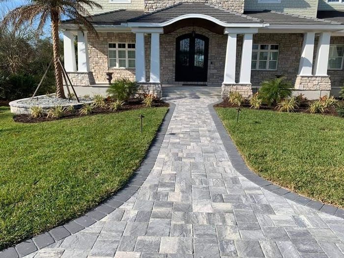 Stone walkway leads to a home’s front entrance with green lawn on both sides.