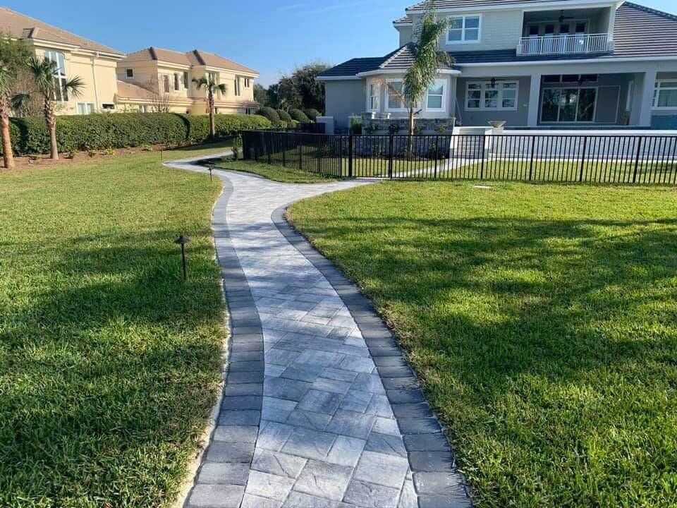 Curved stone walkway through a grassy yard toward a house with a white fence