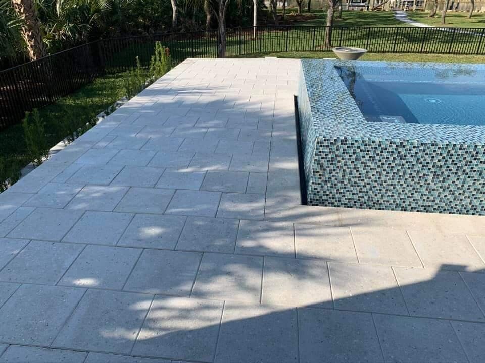 Poolside stone patio beside a blue-tiled swimming pool, with trees and shadows in the background