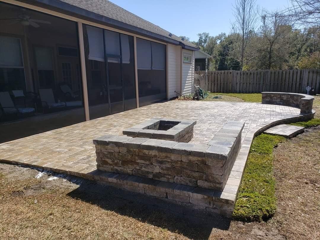 Backyard stone patio with a square fire pit beside a screened porch and fence