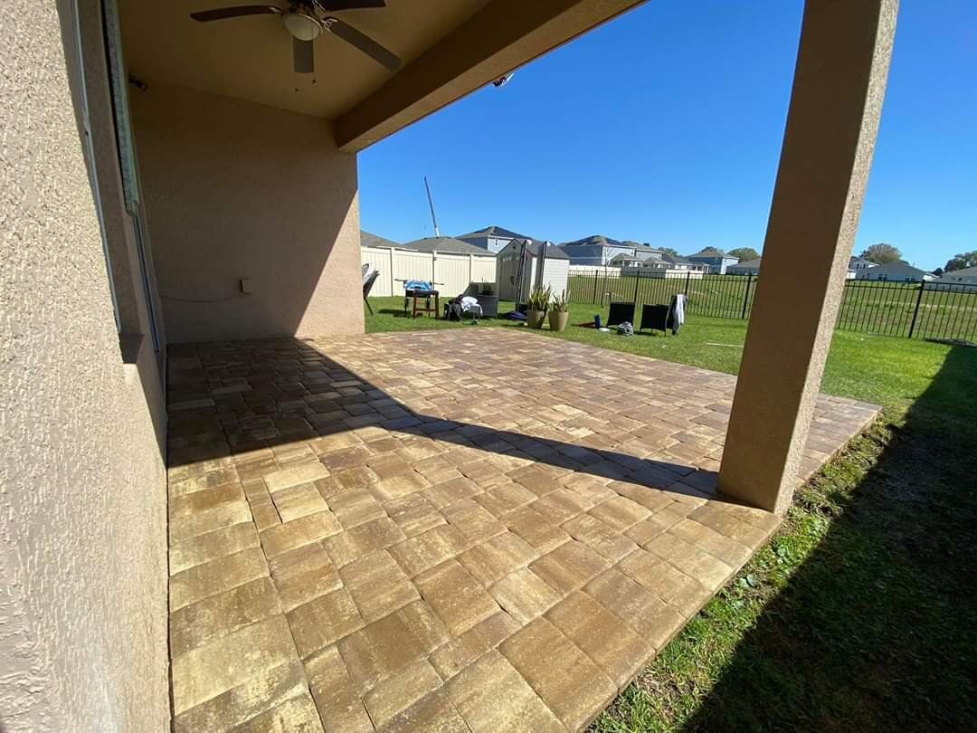 Covered patio with tan pavers overlooking a grassy yard and bright blue sky