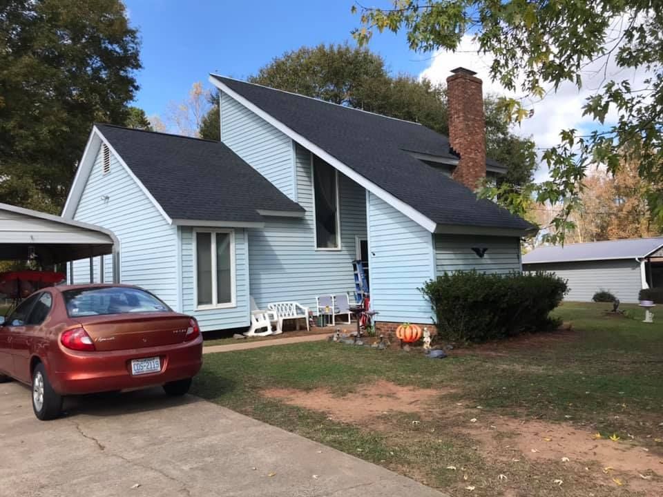 A red car is parked in front of a blue house.